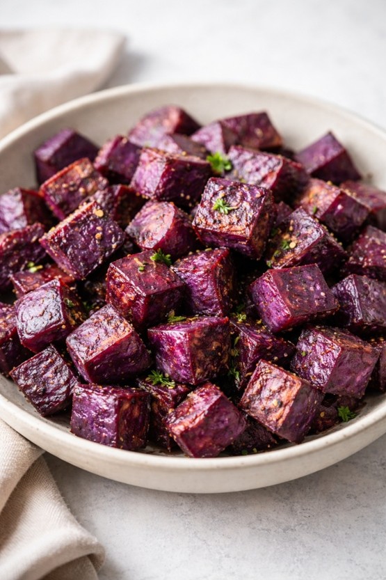 Bowl of roasted purple sweet potato cubes garnished with fresh herbs