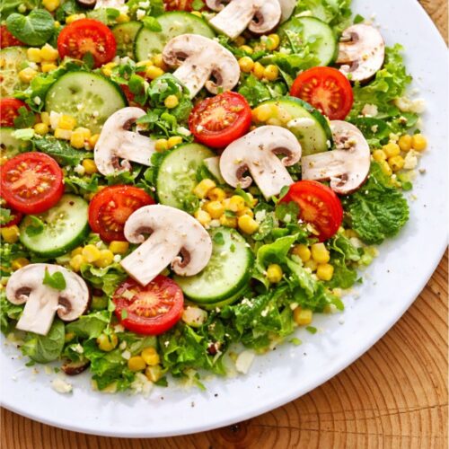 Salad plate with sliced mushrooms, cherry tomatoes, cucumber, and corn on a bed of greens