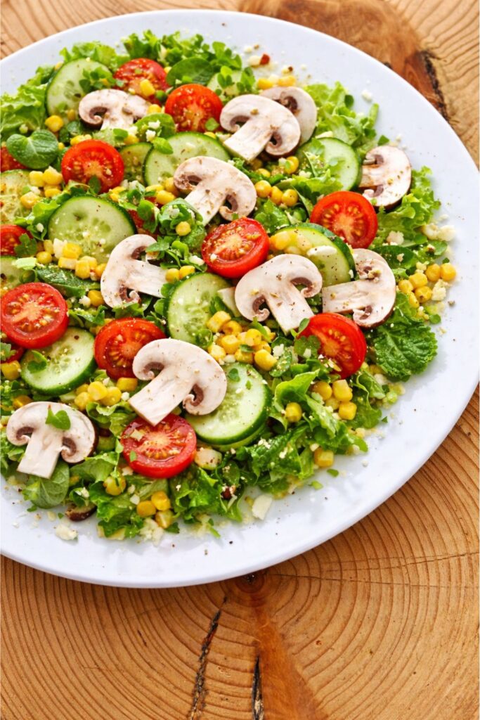 Fresh vegetable salad with mushrooms, tomatoes, cucumbers, and corn on a white plate