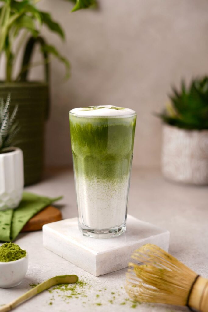 Iced matcha latte with layered green tea and milk in a tall glass, surrounded by potted succulents