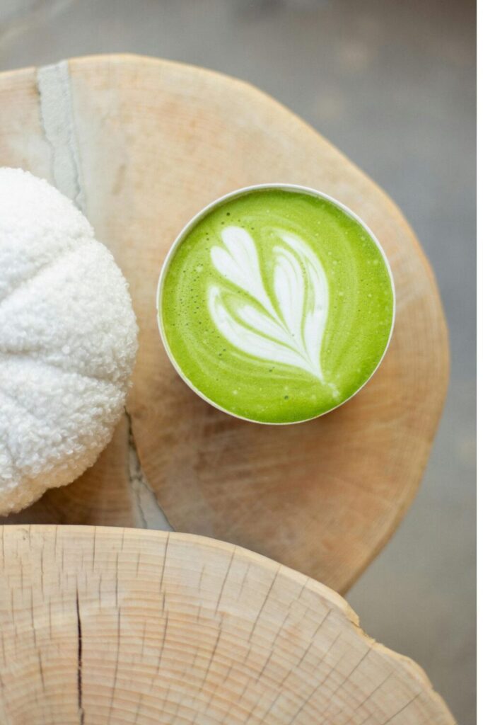 Overhead view of a matcha latte with heart-shaped latte art in a cup on a wooden table