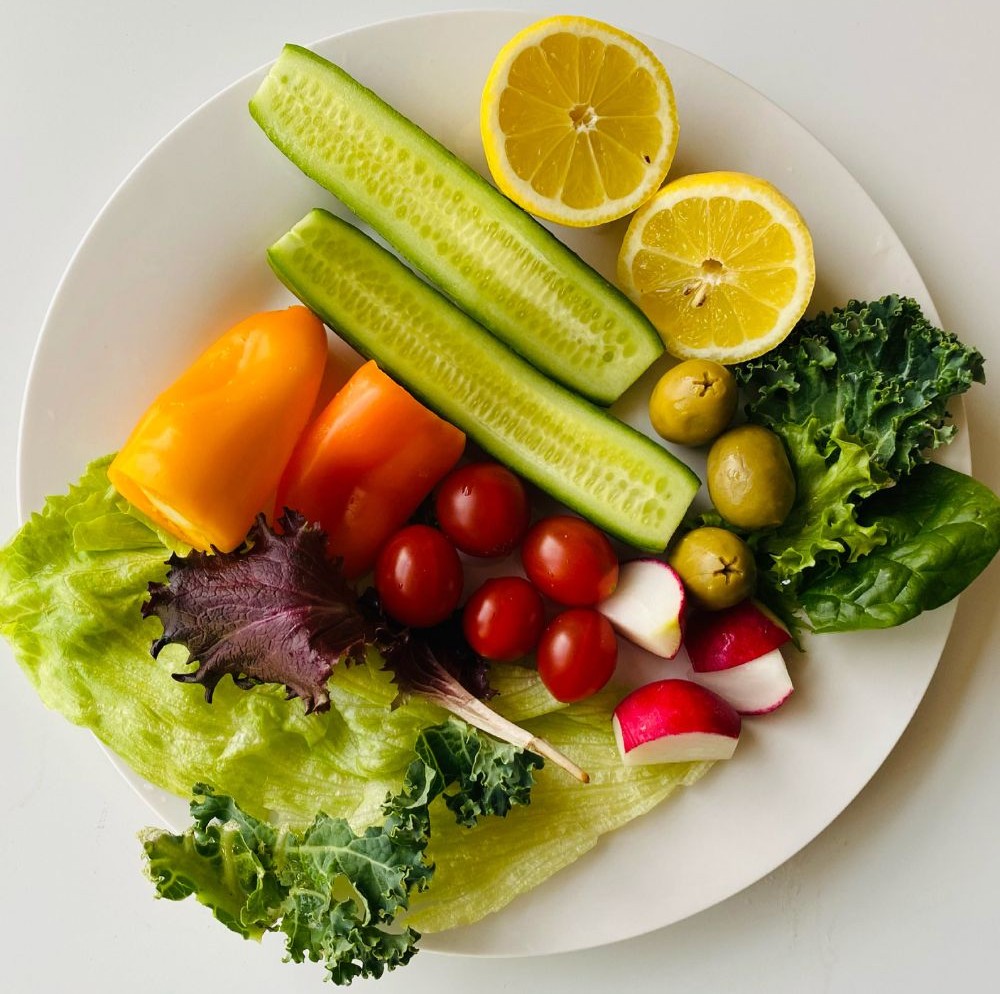 Plate of fresh vegetables including lettuce, tomatoes, cucumber, bell pepper, radish, and olives
