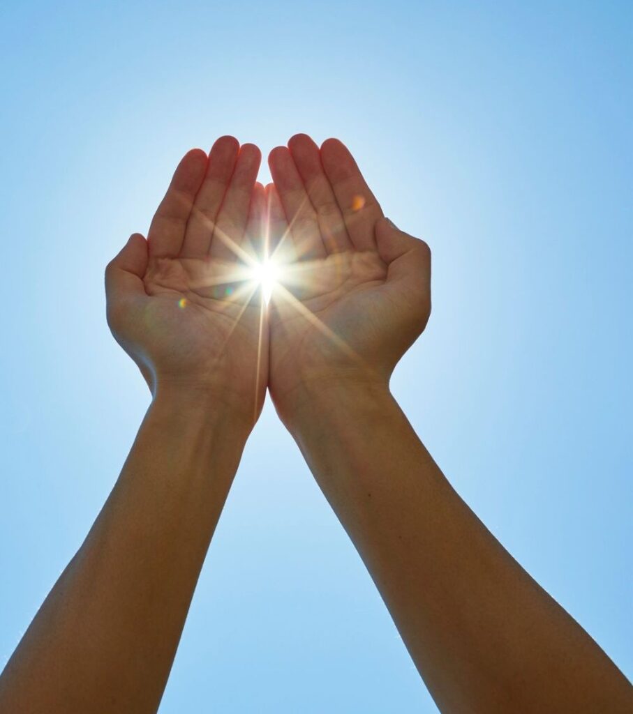 Cupped hands raised toward the sun in a clear blue sky, symbolizing vitamin D and eye health from nutrients found in eggs
