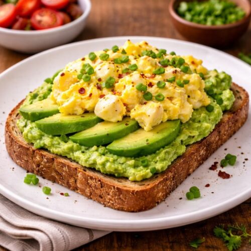 Avocado toast topped with scrambled eggs, peas, and chili flakes, served with tomatoes