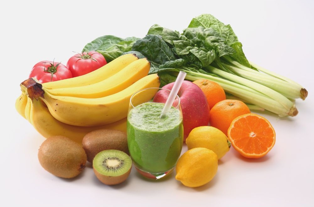 Green smoothie in a glass surrounded by fresh fruits and vegetables