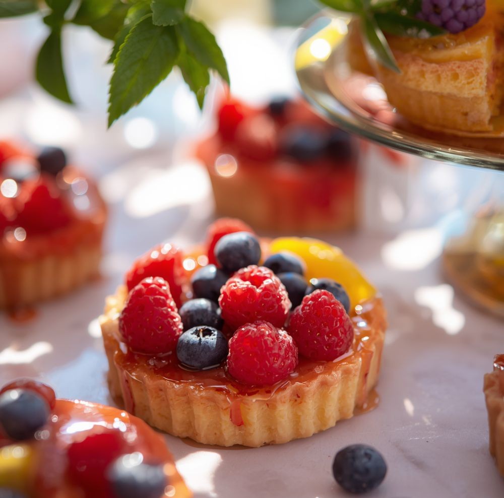 Mini tarts filled with custard and topped with raspberries, blueberries, and mango on a table
