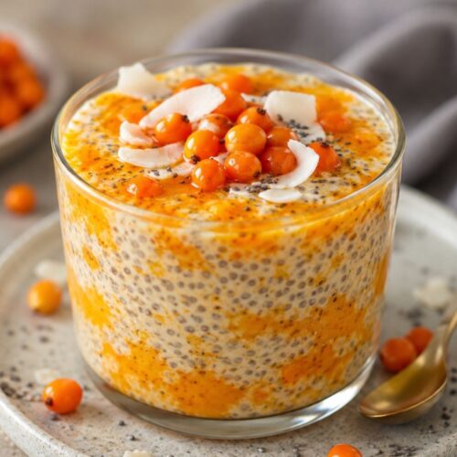Glass of chia seed pudding topped with sea buckthorn berries and coconut flakes