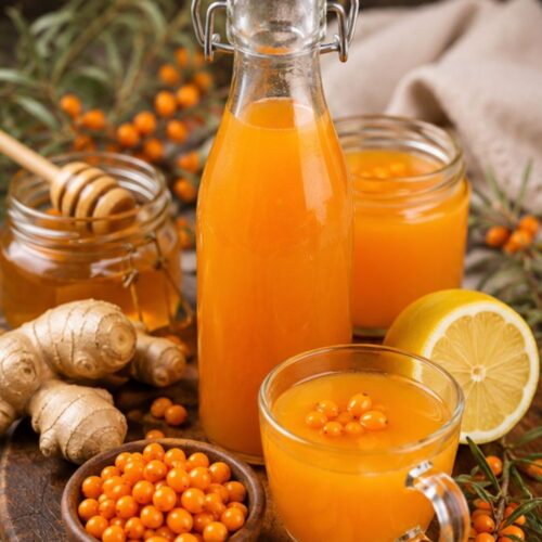 Swing-top bottle of sea buckthorn juice with fresh berries and a green sprig in the background