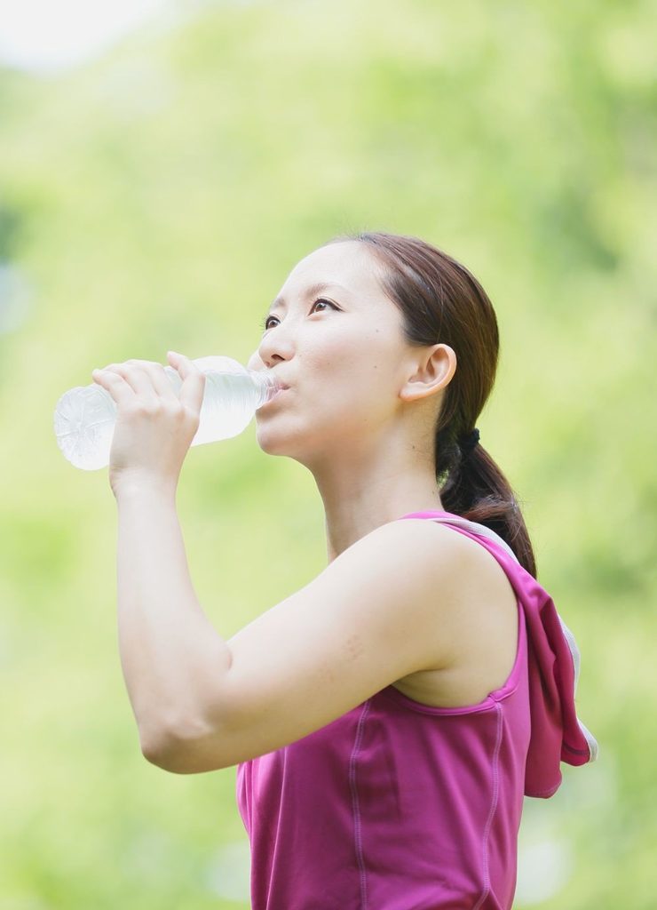 Woman drinking water outdoors after exercise